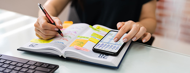 Eine Frau streicht in ihrem Kalender Termine an und vergleicht diese mit ihrem Handy