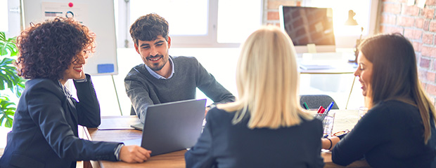 Drei Frauen und ein Mann sitzen an einem Tisch im Büro und unterhalten sich